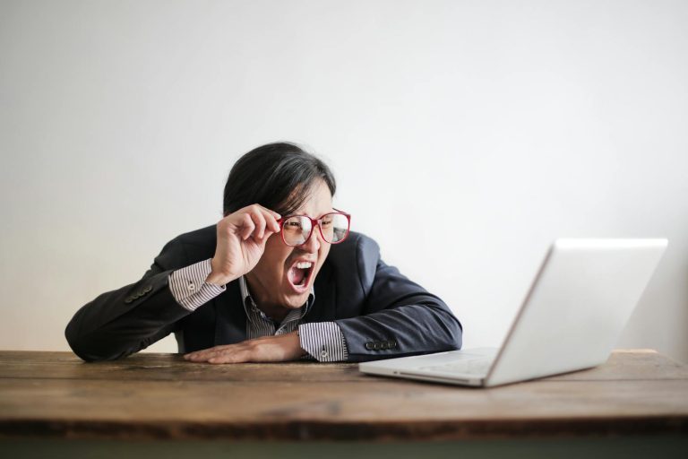 Man in jacket and glasses looking at laptop and screaming